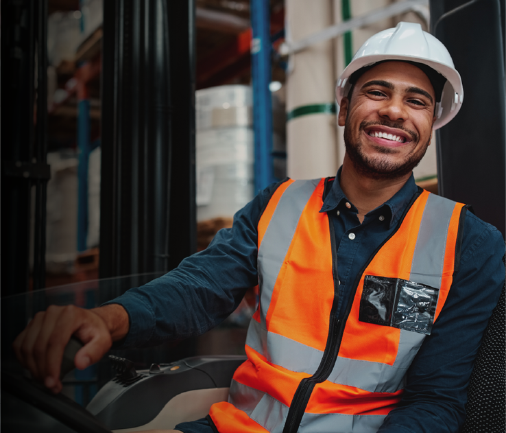 Hombre con casco blanco y chaleco con naranja con reflectivo, sentado y sonriendo