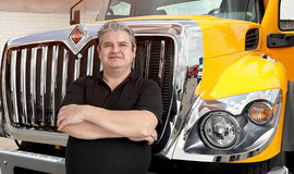 Juan Rueda con los brazos cruzados en frente de un camión INTERNATIONAL® amarillo